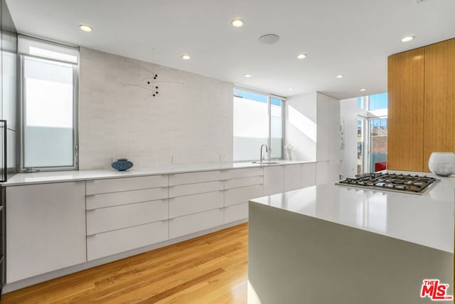 kitchen featuring sink, white cabinetry, plenty of natural light, stainless steel gas stovetop, and light hardwood / wood-style floors