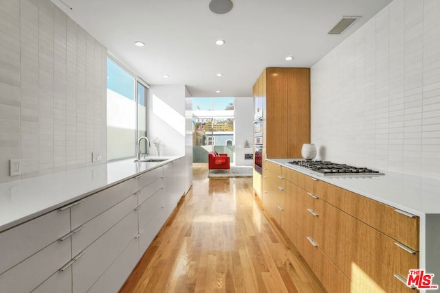 kitchen with sink, light hardwood / wood-style floors, stainless steel gas cooktop, and decorative backsplash