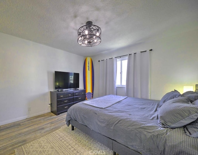 bedroom with a textured ceiling, wood finished floors, and baseboards