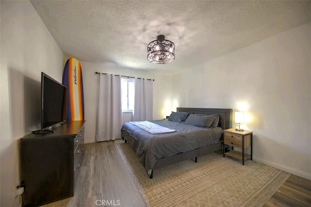 bedroom with a textured ceiling, wood finished floors, and baseboards