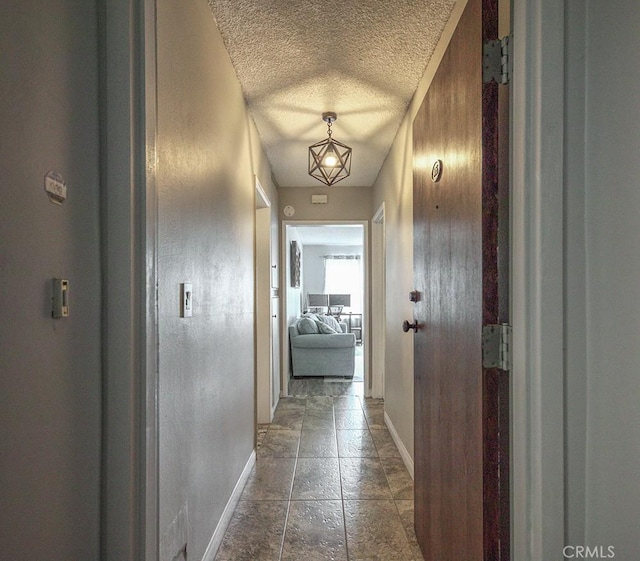 hall featuring stone tile floors, a textured ceiling, and baseboards