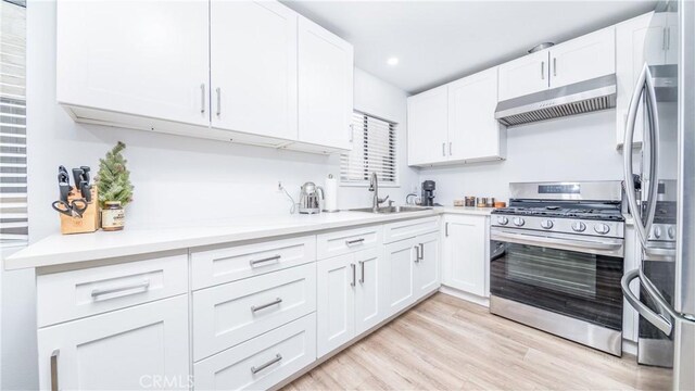 kitchen featuring sink, light hardwood / wood-style flooring, wall chimney range hood, stainless steel appliances, and white cabinets