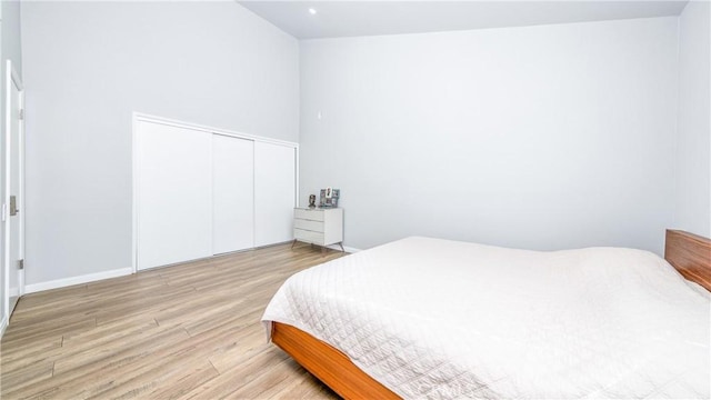 bedroom with a towering ceiling, light hardwood / wood-style floors, and a closet