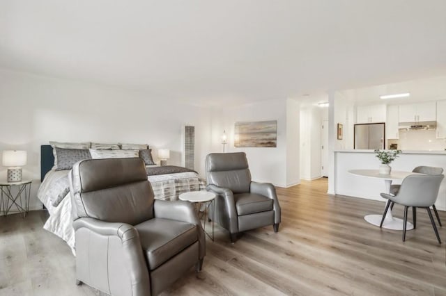 bedroom with stainless steel refrigerator and light hardwood / wood-style floors