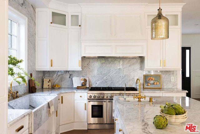 kitchen featuring pendant lighting, white cabinetry, backsplash, light stone countertops, and range with two ovens