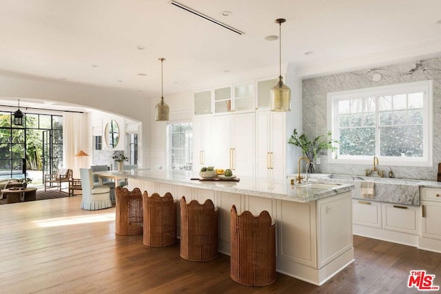 kitchen featuring an island with sink, sink, a breakfast bar area, white cabinets, and light stone countertops