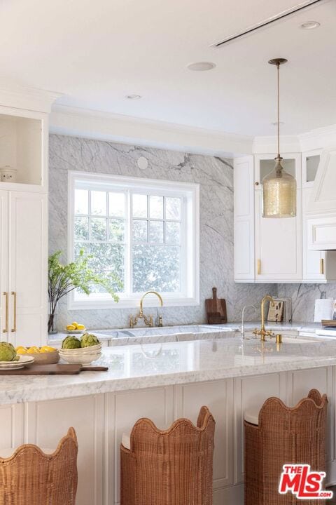 kitchen with pendant lighting, a wealth of natural light, light stone countertops, and white cabinets