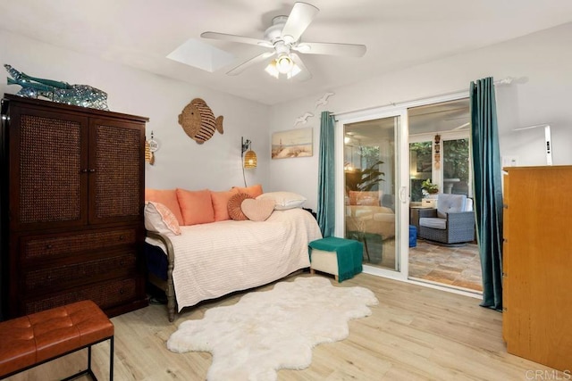 bedroom with a skylight, light hardwood / wood-style floors, ceiling fan, and access to outside