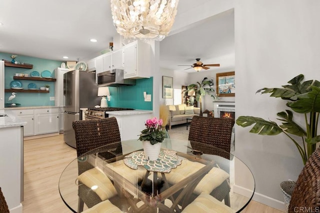 dining space with ceiling fan with notable chandelier and light hardwood / wood-style flooring