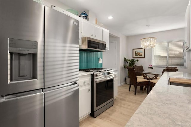 kitchen with white cabinetry, hanging light fixtures, stainless steel appliances, a notable chandelier, and light hardwood / wood-style floors