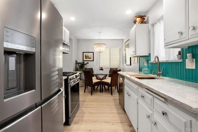 kitchen featuring sink, white cabinetry, decorative light fixtures, light hardwood / wood-style flooring, and stainless steel appliances