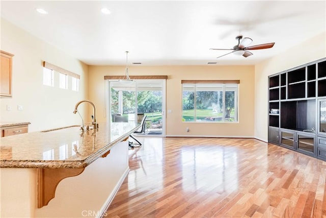 9431 Hughes Dr, Corona, CA 92883 - kitchen featuring light stone counters, hanging light fixtures, light wood-style floors, a sink, and baseboards