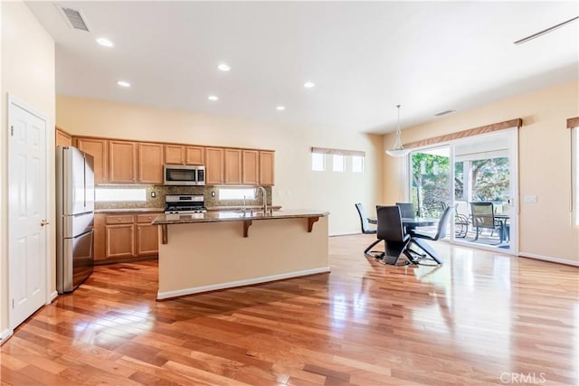 9431 Hughes Dr, Corona, CA 92883 - kitchen with stainless steel appliances, light wood-style floors, backsplash, and a kitchen breakfast bar