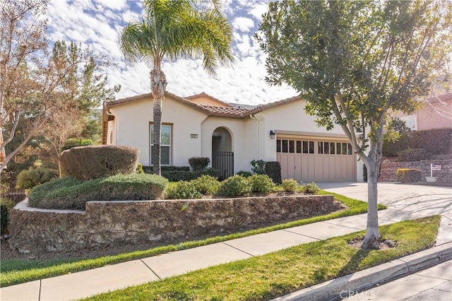 mediterranean / spanish-style house with an attached garage, a tile roof, concrete driveway, and stucco siding