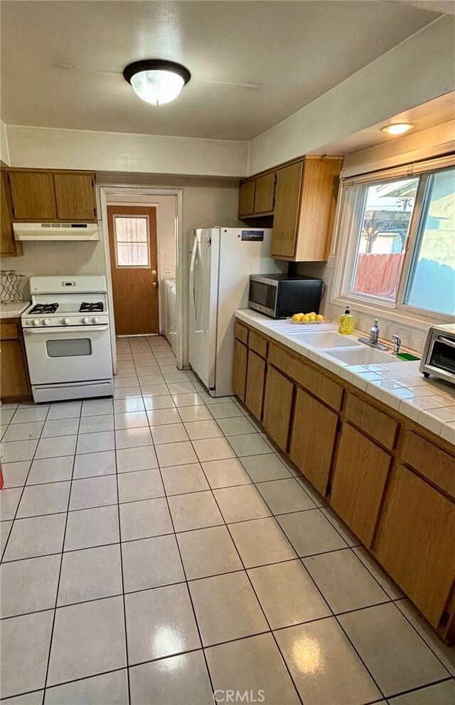 kitchen with sink, decorative backsplash, light tile patterned floors, tile counters, and white appliances