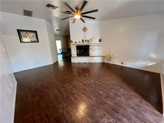 unfurnished living room with ceiling fan, dark hardwood / wood-style flooring, and a stone fireplace