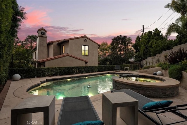 pool at dusk featuring a patio and an in ground hot tub