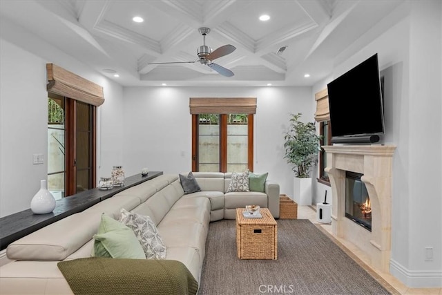 living room with coffered ceiling, ceiling fan, a premium fireplace, and beamed ceiling