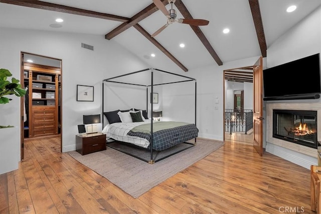 bedroom with lofted ceiling with beams, a multi sided fireplace, and light hardwood / wood-style flooring