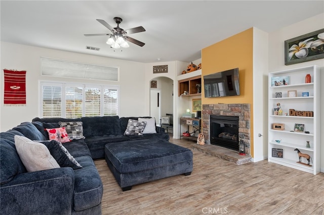 living room featuring built in shelves, ceiling fan, a stone fireplace, and hardwood / wood-style floors