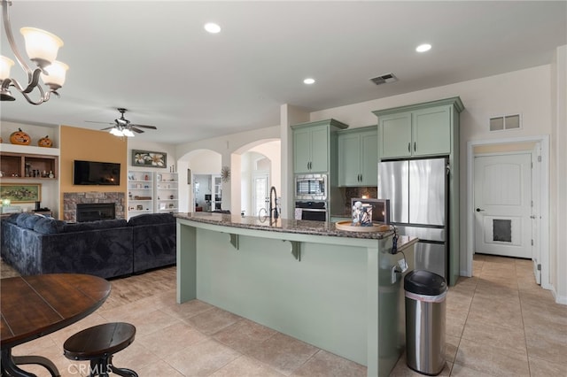 kitchen with appliances with stainless steel finishes, a stone fireplace, pendant lighting, a kitchen breakfast bar, and green cabinets