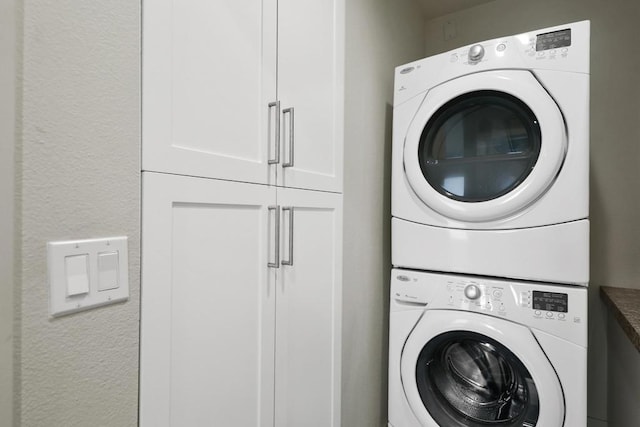 clothes washing area with cabinets and stacked washing maching and dryer