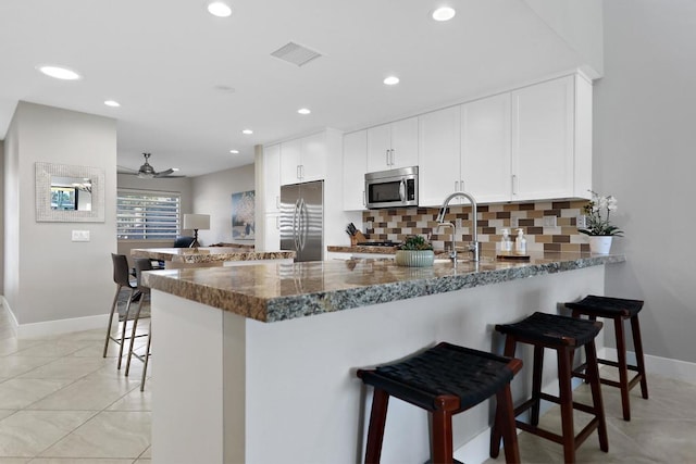 kitchen featuring a breakfast bar, appliances with stainless steel finishes, white cabinetry, dark stone countertops, and kitchen peninsula