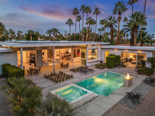 back house at dusk featuring an in ground hot tub, a patio, and a fire pit