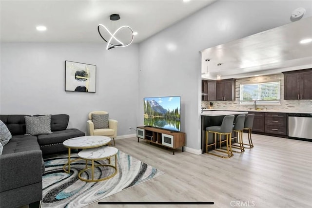 living room with an inviting chandelier, sink, and light hardwood / wood-style flooring