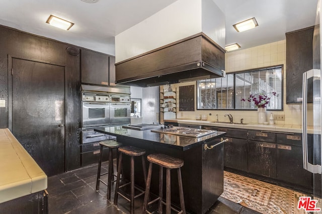 kitchen featuring dark brown cabinetry, stainless steel gas stovetop, sink, and a kitchen island