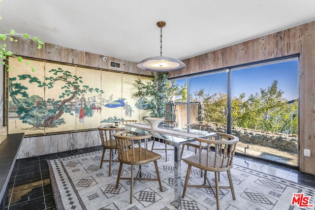 dining area featuring wooden walls and dark tile patterned flooring