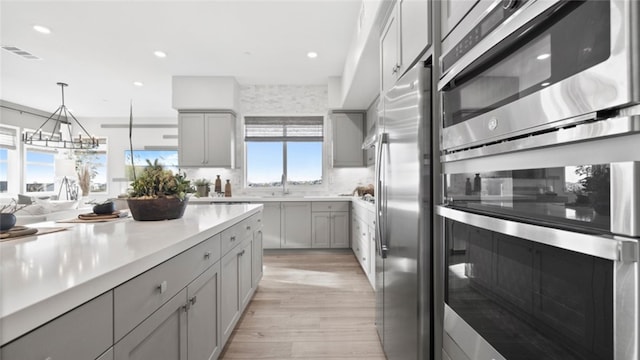 kitchen featuring sink, gray cabinetry, light wood-type flooring, pendant lighting, and stainless steel appliances