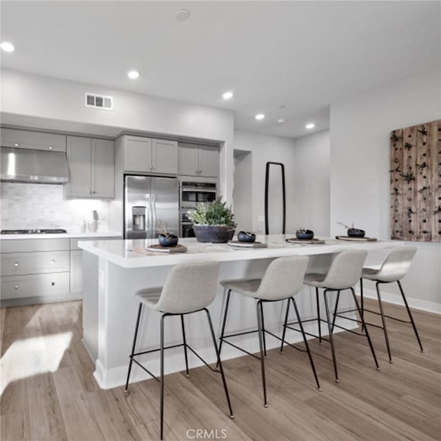 kitchen with built in fridge, gray cabinetry, a kitchen breakfast bar, a large island, and wall chimney range hood