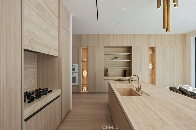 kitchen with white double oven, sink, light hardwood / wood-style flooring, and light brown cabinets