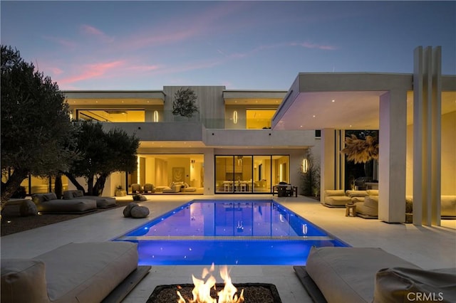 back of house at dusk featuring stucco siding, an outdoor living space with a fire pit, an outdoor pool, and a patio