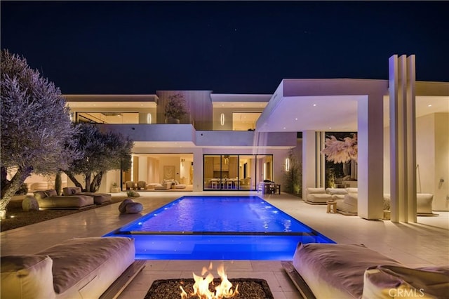 pool at night with an outdoor living space with a fire pit, an infinity pool, and a patio area