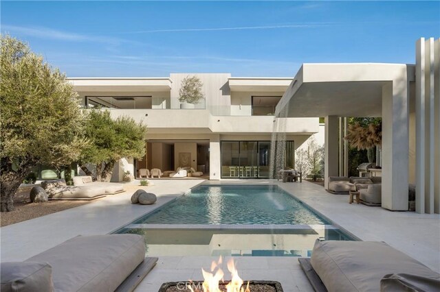 rear view of house featuring a balcony, a patio area, pool water feature, and an outdoor fire pit