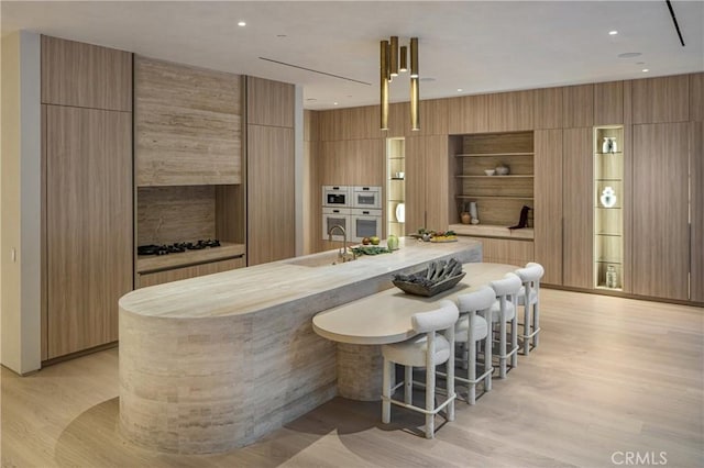 kitchen with a large island, a breakfast bar area, hanging light fixtures, double oven, and light hardwood / wood-style floors