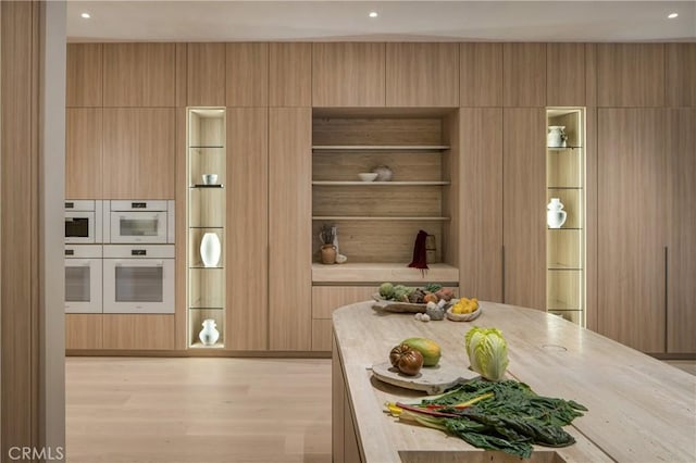 kitchen featuring butcher block counters, double oven, light brown cabinets, and light wood-type flooring