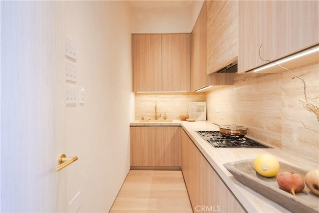 kitchen featuring a sink, light countertops, decorative backsplash, light brown cabinetry, and stainless steel gas stovetop