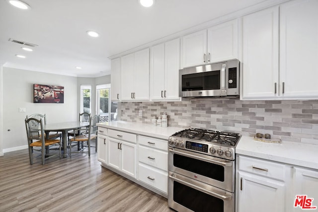 kitchen with crown molding, light hardwood / wood-style flooring, appliances with stainless steel finishes, white cabinetry, and tasteful backsplash