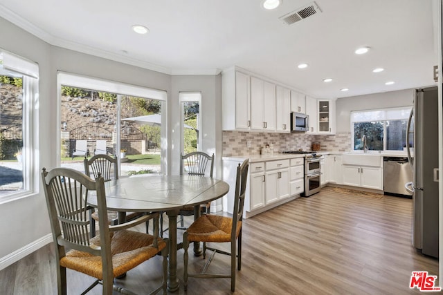 kitchen with appliances with stainless steel finishes, tasteful backsplash, white cabinetry, ornamental molding, and light wood-type flooring