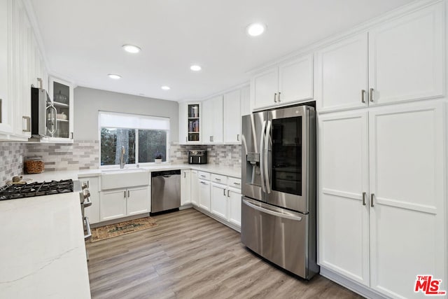 kitchen featuring sink, white cabinets, light stone counters, stainless steel appliances, and light hardwood / wood-style flooring