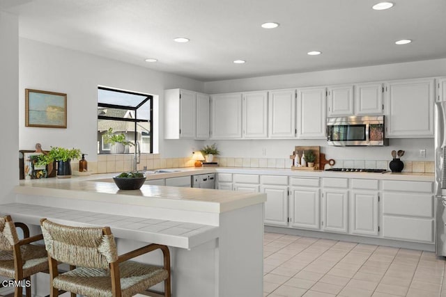 kitchen featuring sink, white cabinetry, a kitchen breakfast bar, stainless steel appliances, and kitchen peninsula