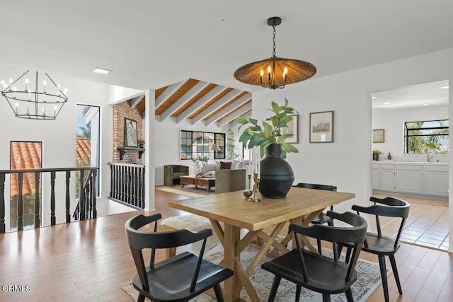 dining space featuring vaulted ceiling with beams, sink, an inviting chandelier, and light hardwood / wood-style flooring