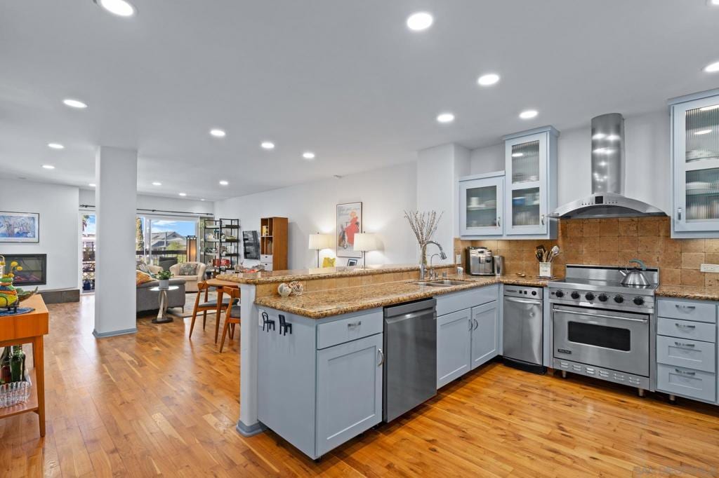 kitchen with sink, kitchen peninsula, wall chimney exhaust hood, and appliances with stainless steel finishes