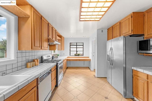 kitchen featuring stainless steel appliances, tile counters, decorative backsplash, and light tile patterned floors