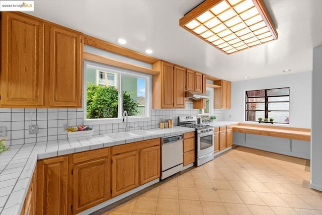 kitchen with gas stove, sink, tile counters, and white dishwasher