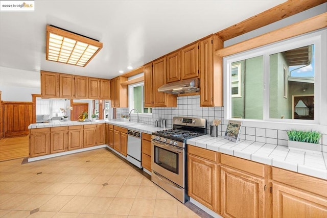 kitchen with dishwasher, sink, backsplash, tile counters, and gas stove