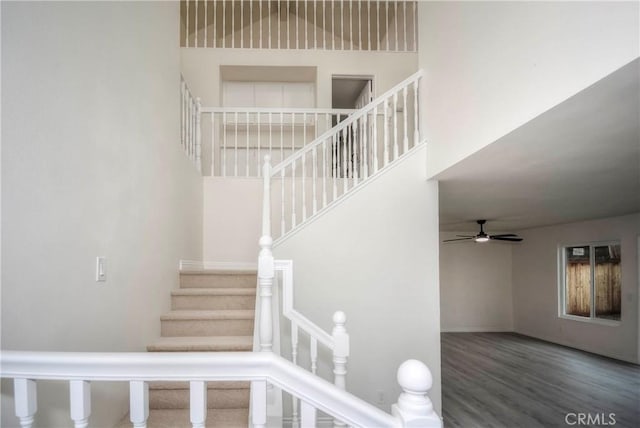 stairway with a towering ceiling, hardwood / wood-style floors, and ceiling fan